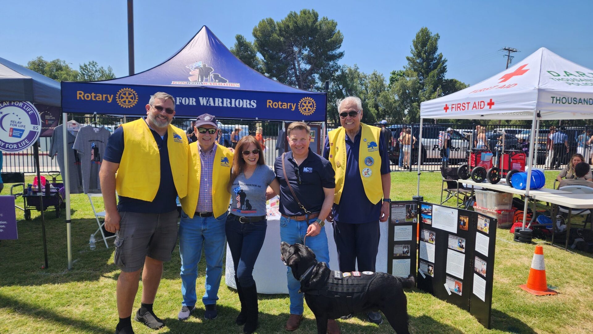 Volunteers in Rotary vests standing with a service dog at an outdoor K9s For Warriors community event